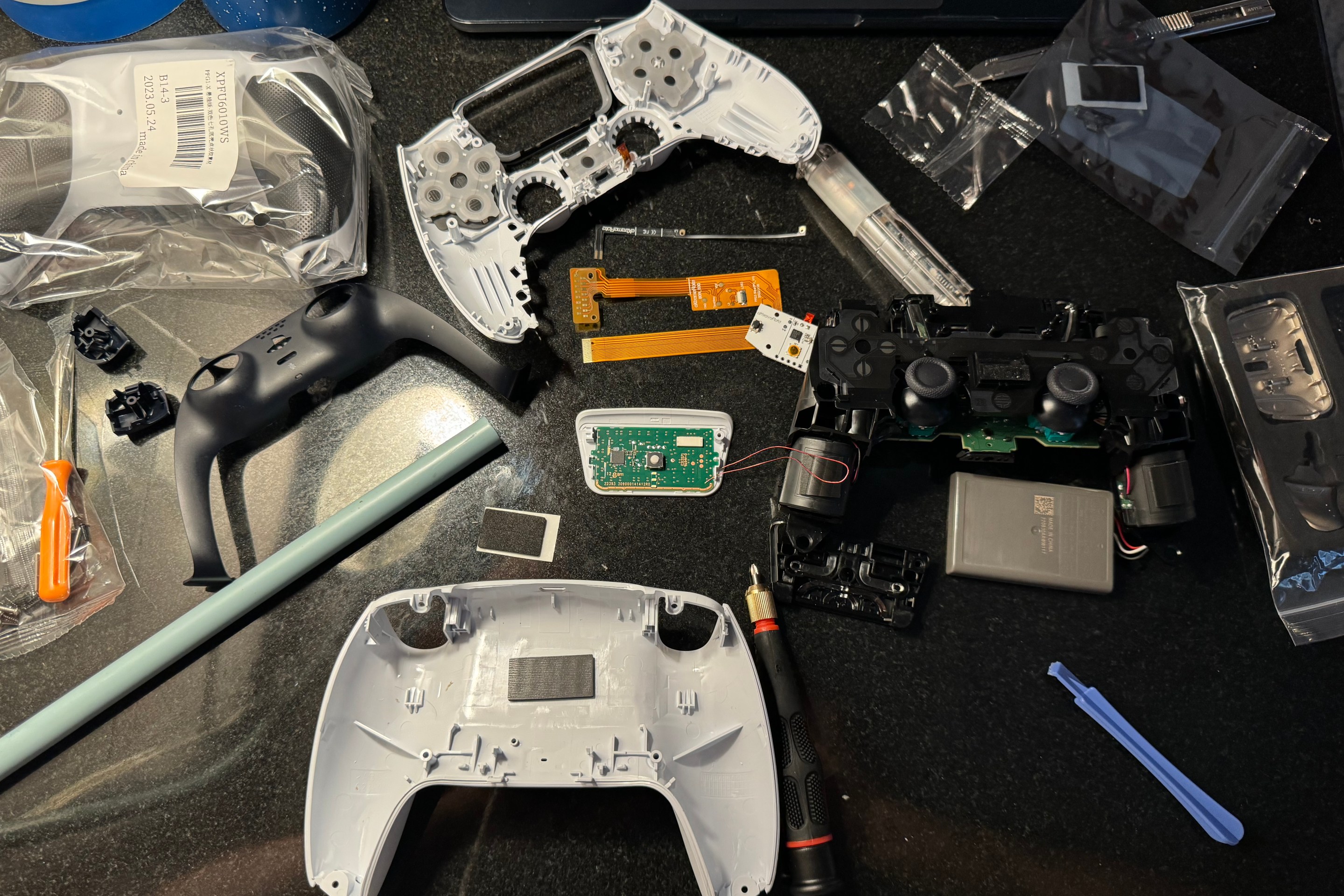 A DualSense controller laid out on a table mid-mod next to a soldering iron and small screwdriver.