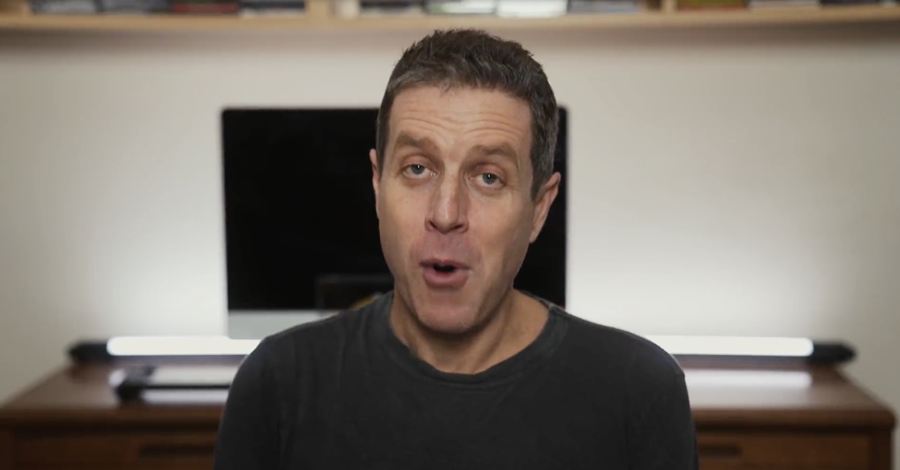 Geoff Keighley, a white man with brown hair, looks excited while sitting in front of a turned-off computer monitor
