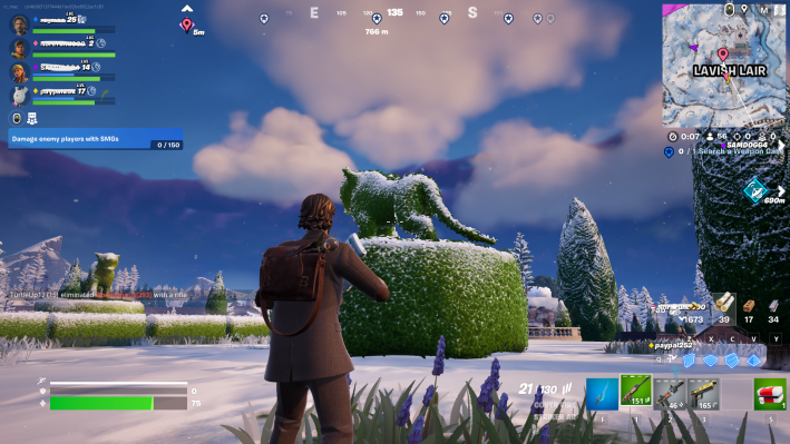 Alan Wake in Fortnite, staring at a green shrub trimmed to resemble a cougar. There is snow on the ground and trees around him.