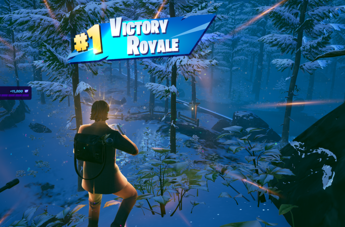 Alan Wake in Fortnite, winning a match standing in a snowy woods. There's a golden glow around him. White and gold text on a blue banner on-screen reads "#1 Victory Royale"