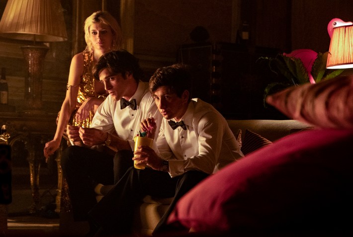 A screenshot from Saltburn. Characters Venetia, Felix and Oliver are wearing formal wear in a dark dining room. They leer at the camera with a but of suspicion.