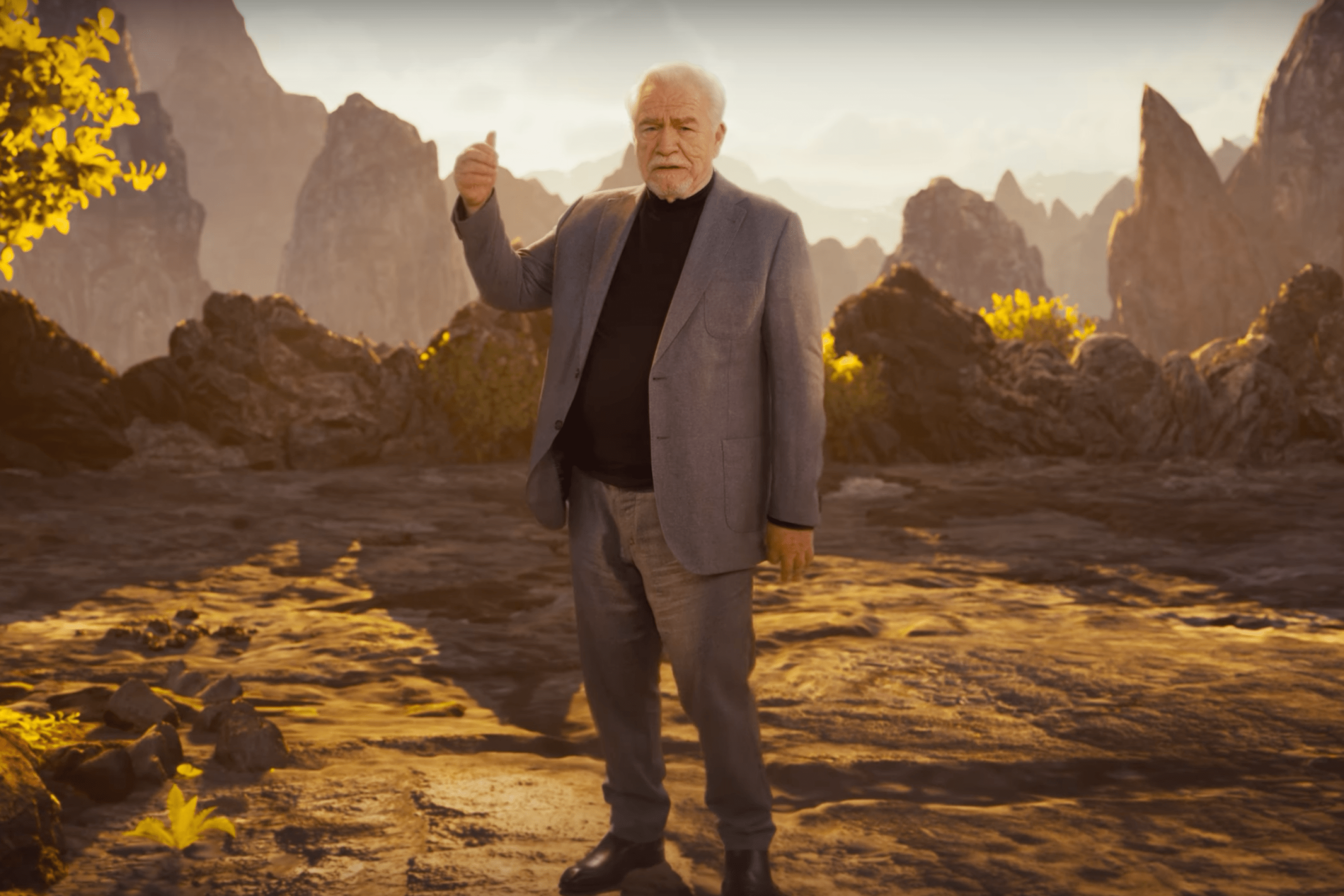Brian Cox, gesturing behind him at a green screen set that depicts a cliff that Heihachi dropped his son off of.