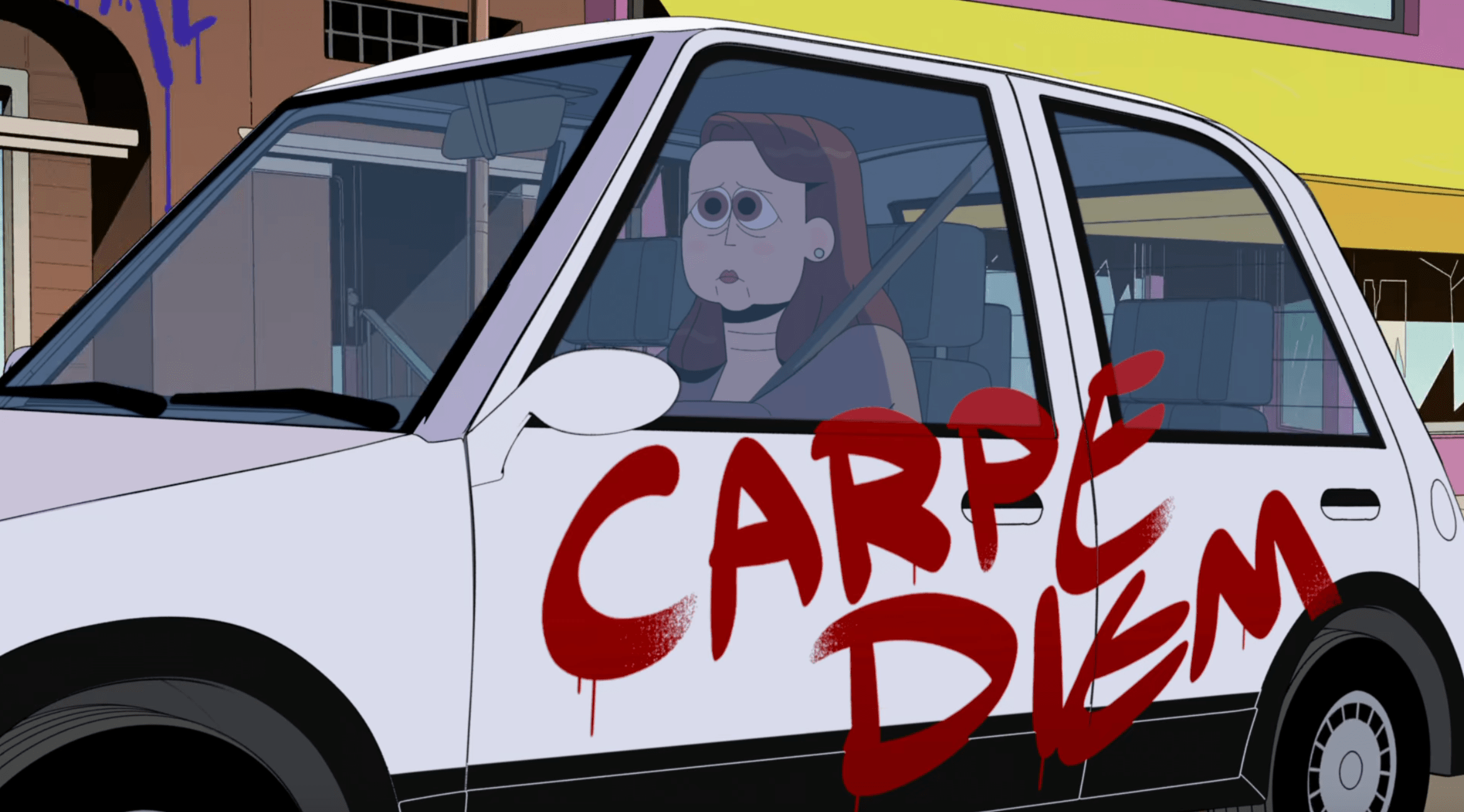 A screenshot from "Carol and the End of the World:" a white woman with brown hair looks sad as she drives a white car with the words "carpe diem" spraypainted in red on the side