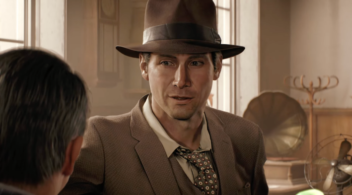 A screenshot from video game Indiana Jones and the Great Circle: Indiana Jones in a brown hat, brown suit coat, white shirt, and brown tie with white spots, standing in an office