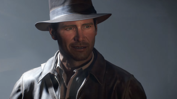 A screenshot from video game Indiana Jones and the Great Circle: Indiana Jones in a brown hat, brown coat, and white shirt, smirking in front of a grey background