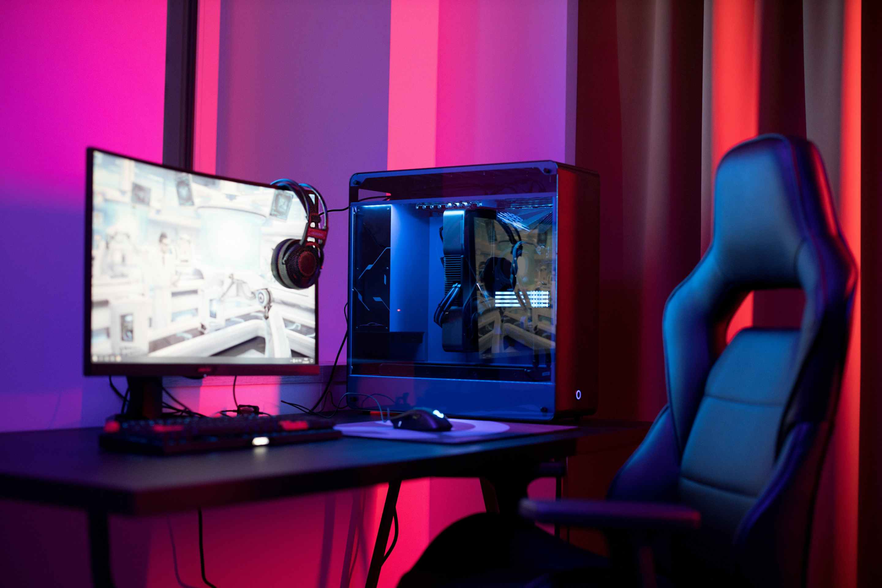 A gaming PC with a clear side sits on a desk, besides a glowing monitor and padded gaming chair