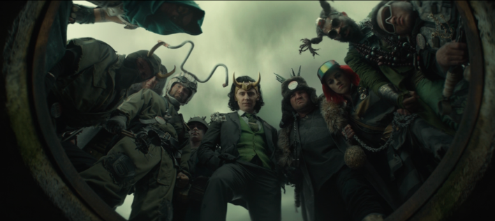 A screenshot from the TV show Loki: ten characters peer into a hole