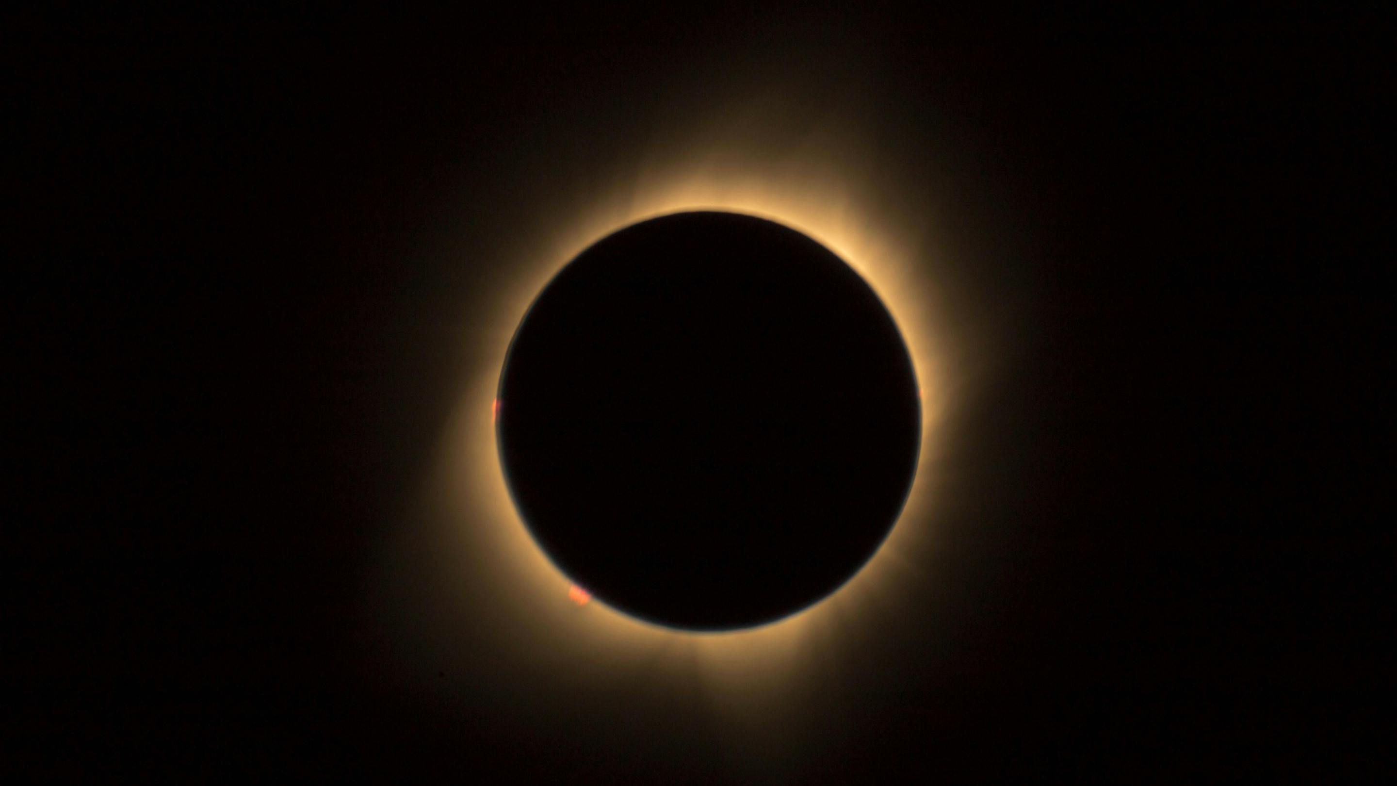 An image of a solar eclipse: a round black moon over a yellow sun, on a black background