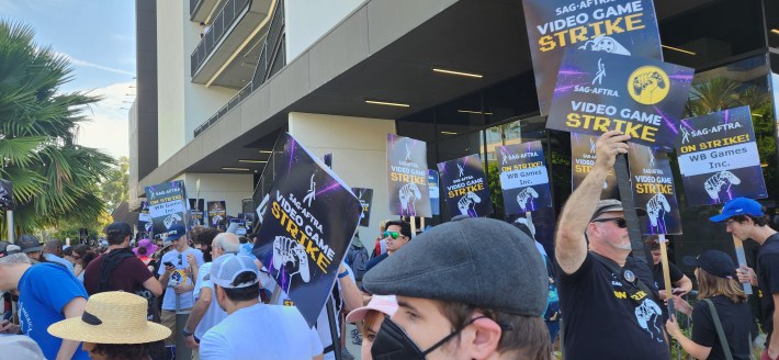 Video game performers picket outside of WB Studios in Burbank, holding signs that read "SAG-AFTRA on strike"