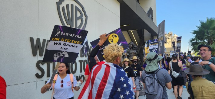 Video game performers picket outside of WB Studios in Burbank, holding signs that read "SAG-AFTRA on strike"