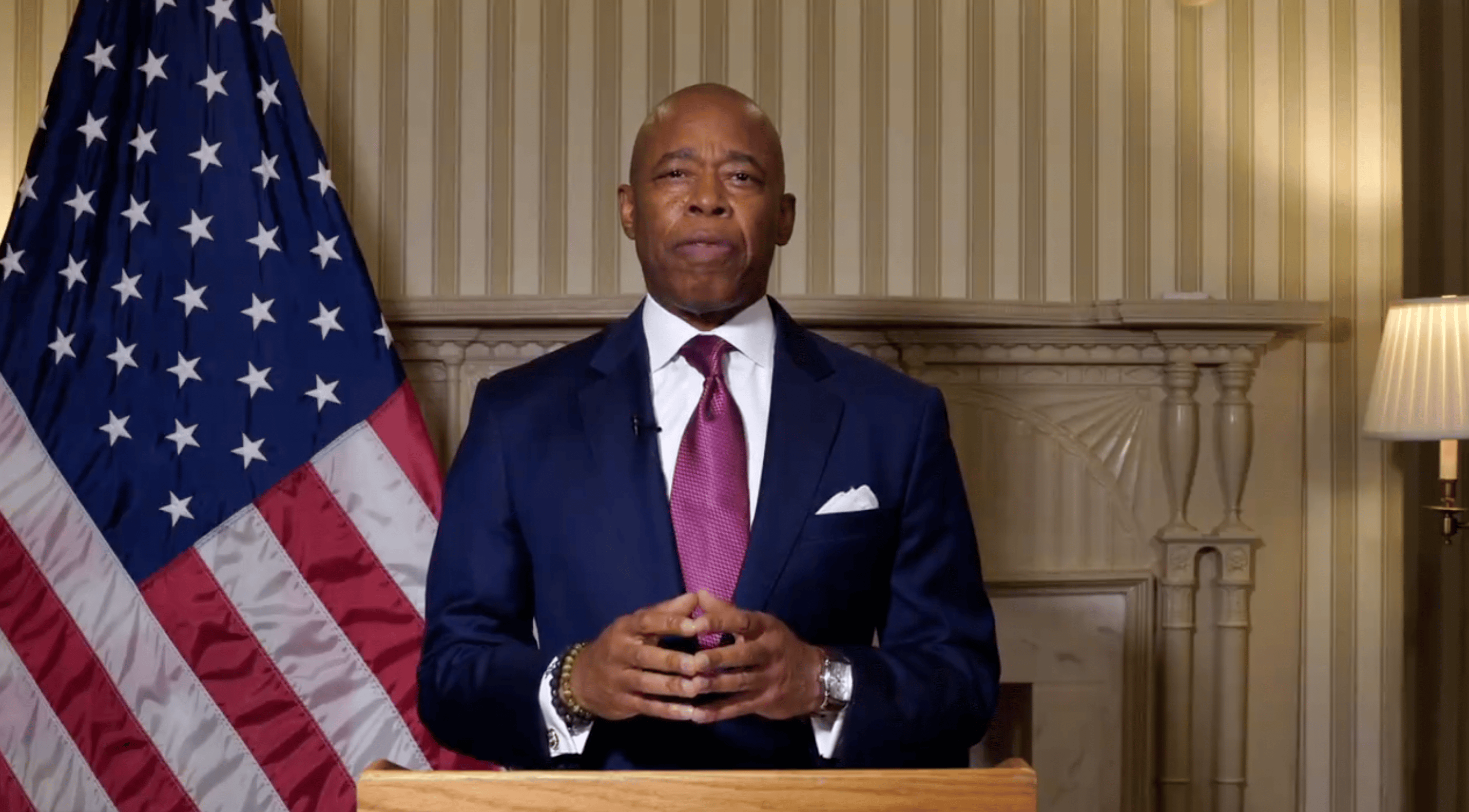 NYC Mayor Eric Adams stands behind a podium next to an American flag