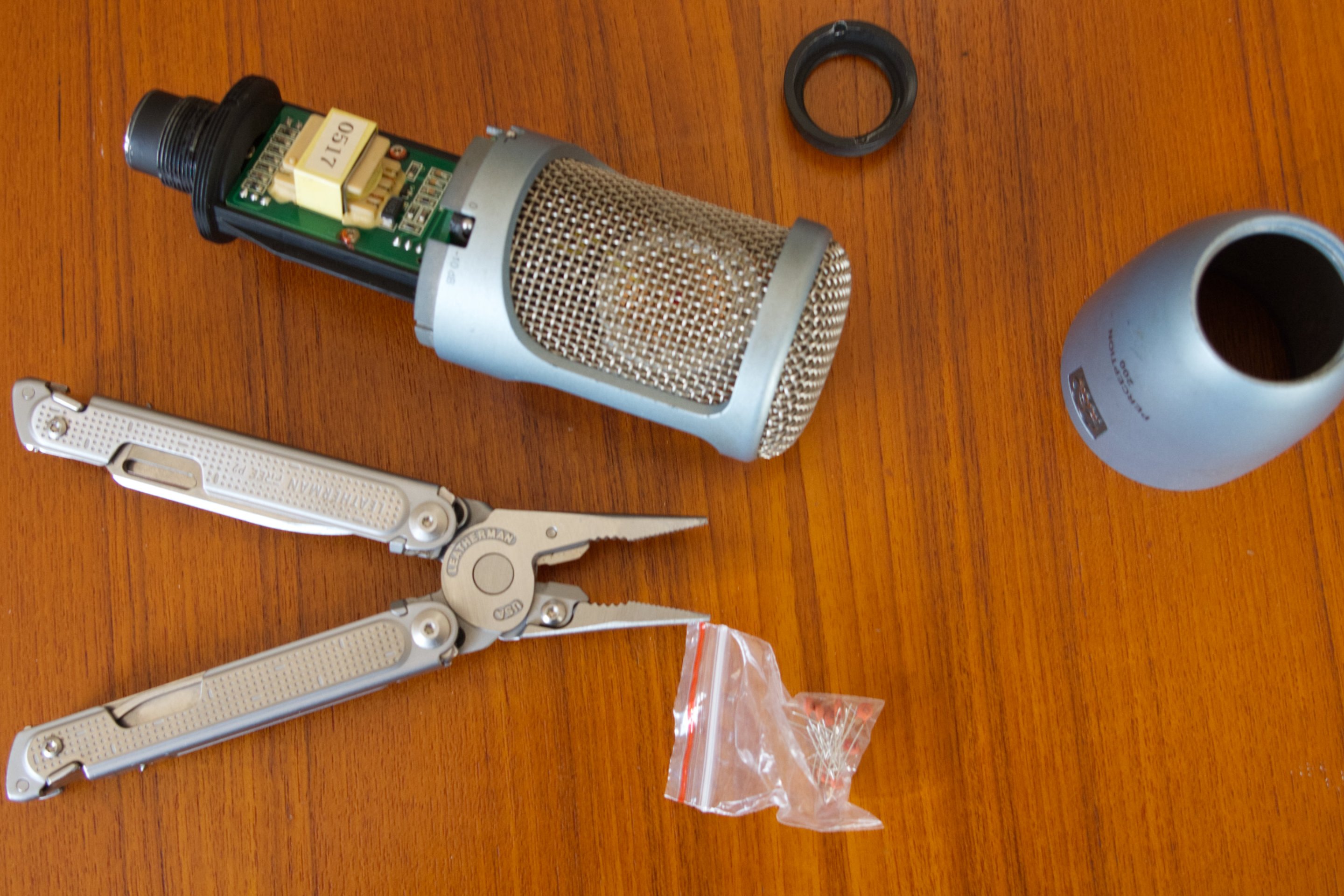 A slightly disassembled AKG Perception 200, next to a pair of pliers and a bag of cheap film capacitors.