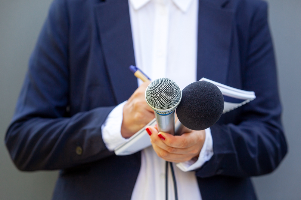 A person in a suit holding a microphone and notepad