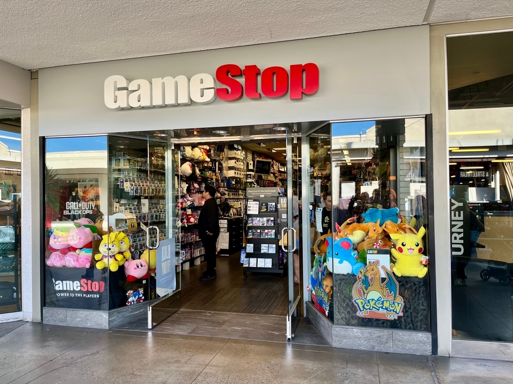 A photograph of a GameStop in a shopping center, showing lots of Pokemon plush toys in the window