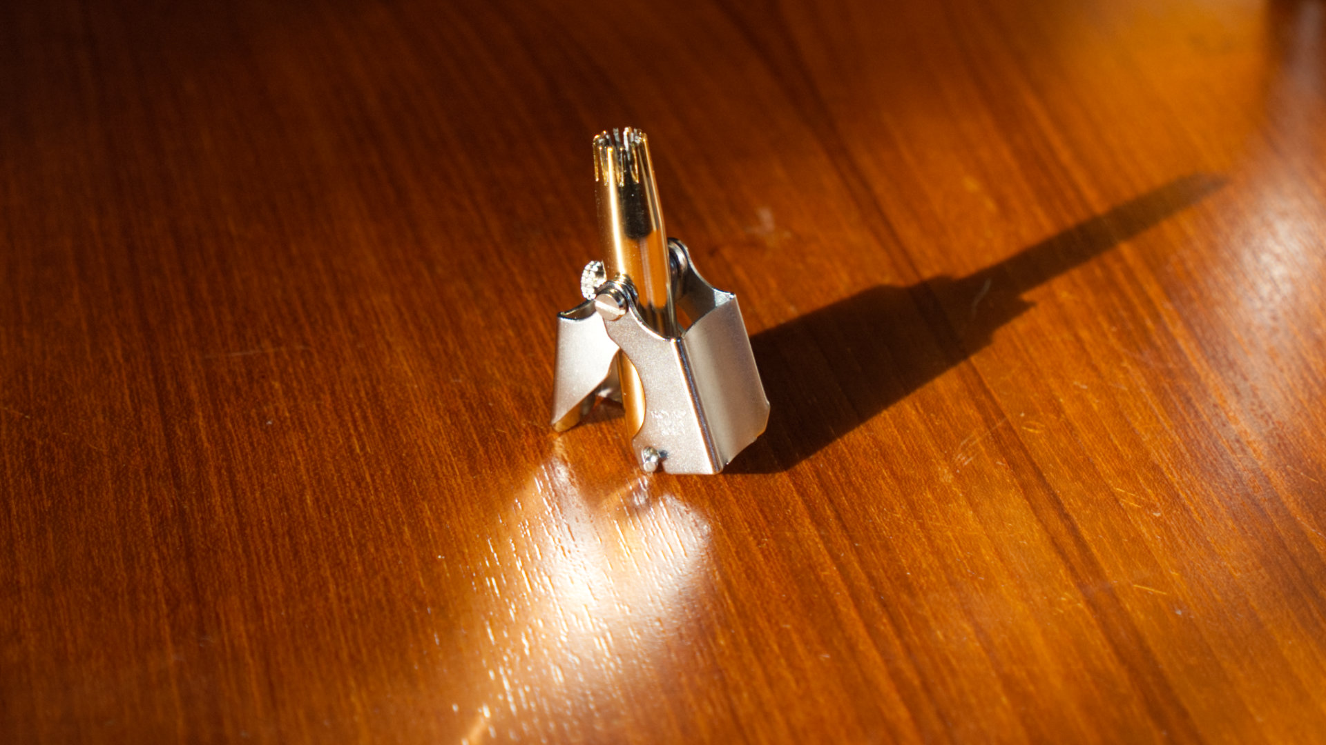 An angelically framed photo of the Golden Birdie nose and ear hair trimmer from Royal. It casts a dramatic shadow and light bounces off of it on to the wooden surface.